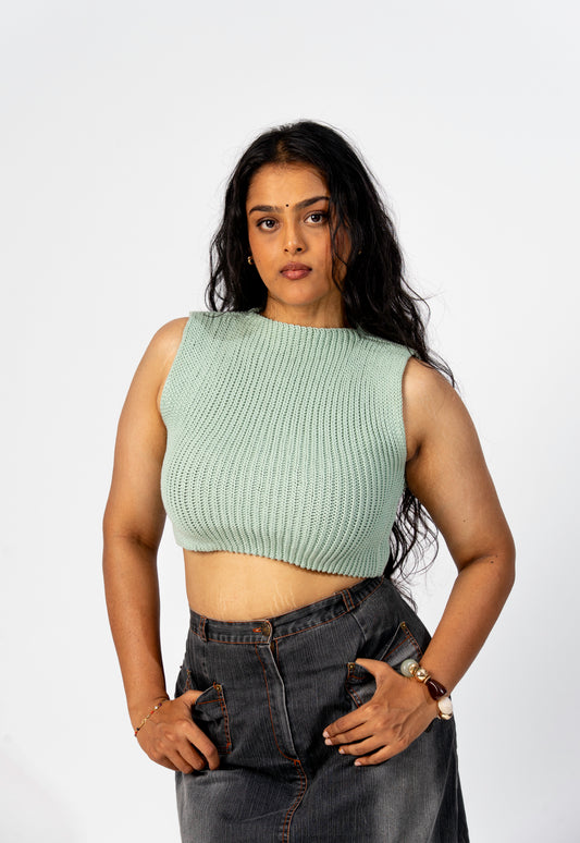 Woman wearing a light sage green sleeveless top and dark jeans on a white background