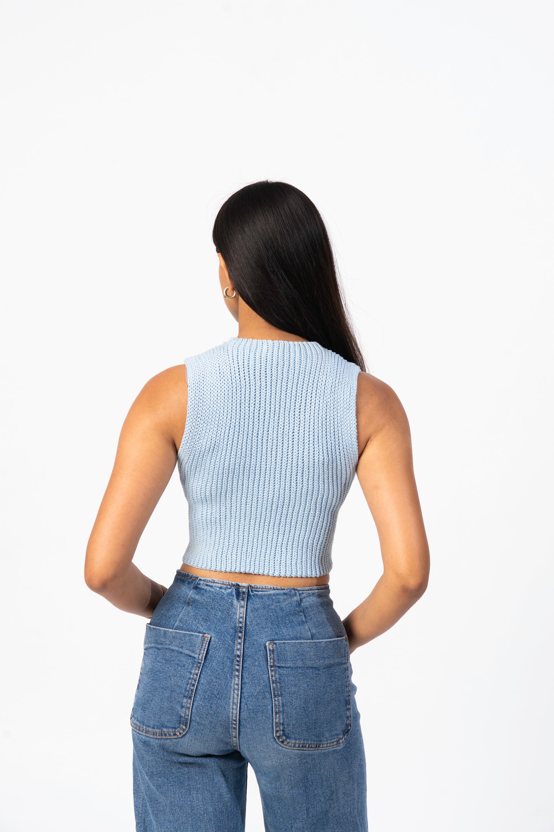 Person wearing a light blue ribbed tank top and blue jeans on a white background