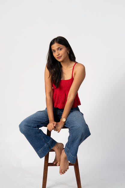Woman sitting on a stool wearing a red top and blue jeans against a white background