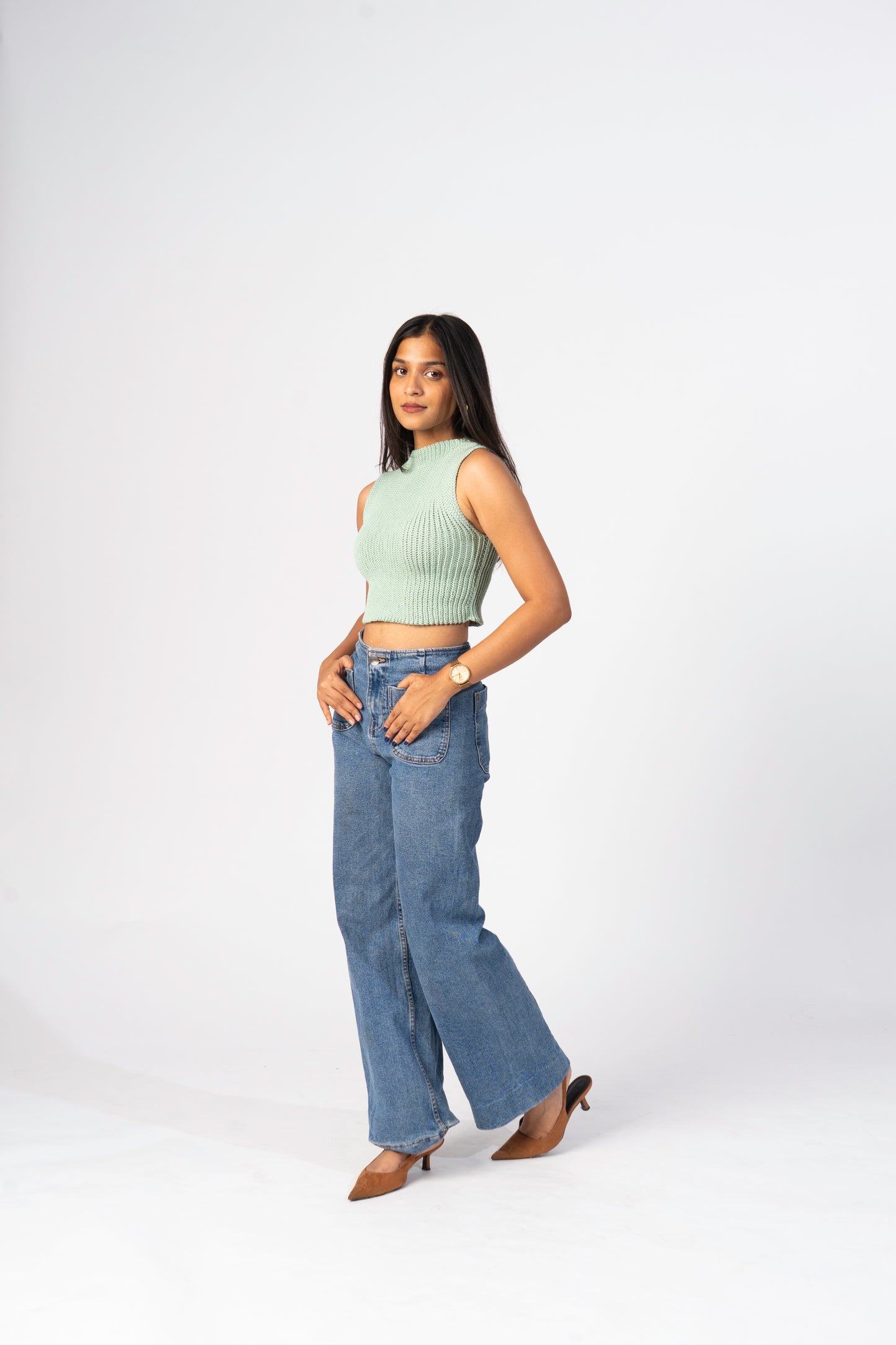 Woman wearing a light green sleeveless top and blue jeans on a white background