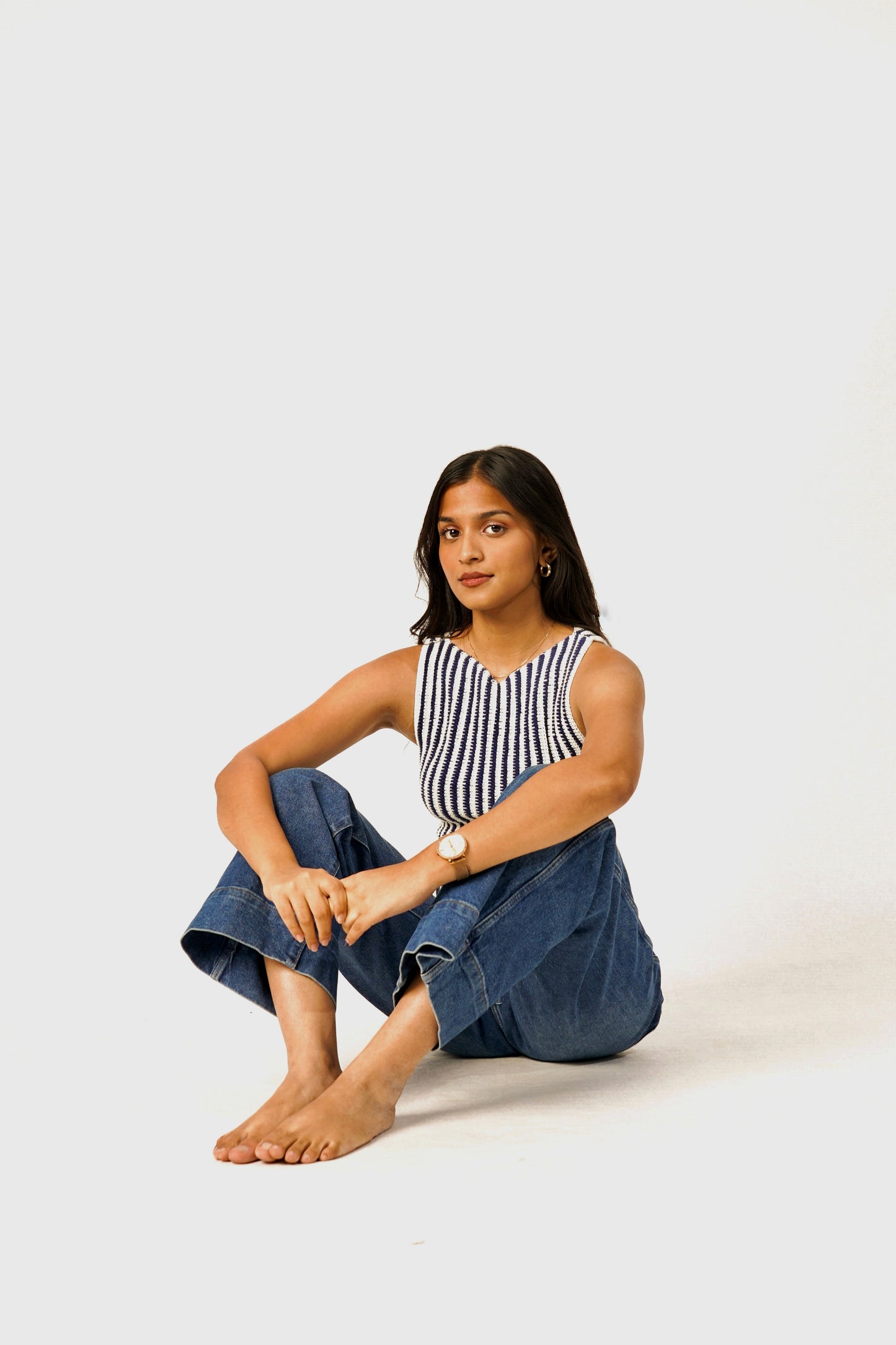Woman sitting on a white background wearing a striped top and blue jeans.
